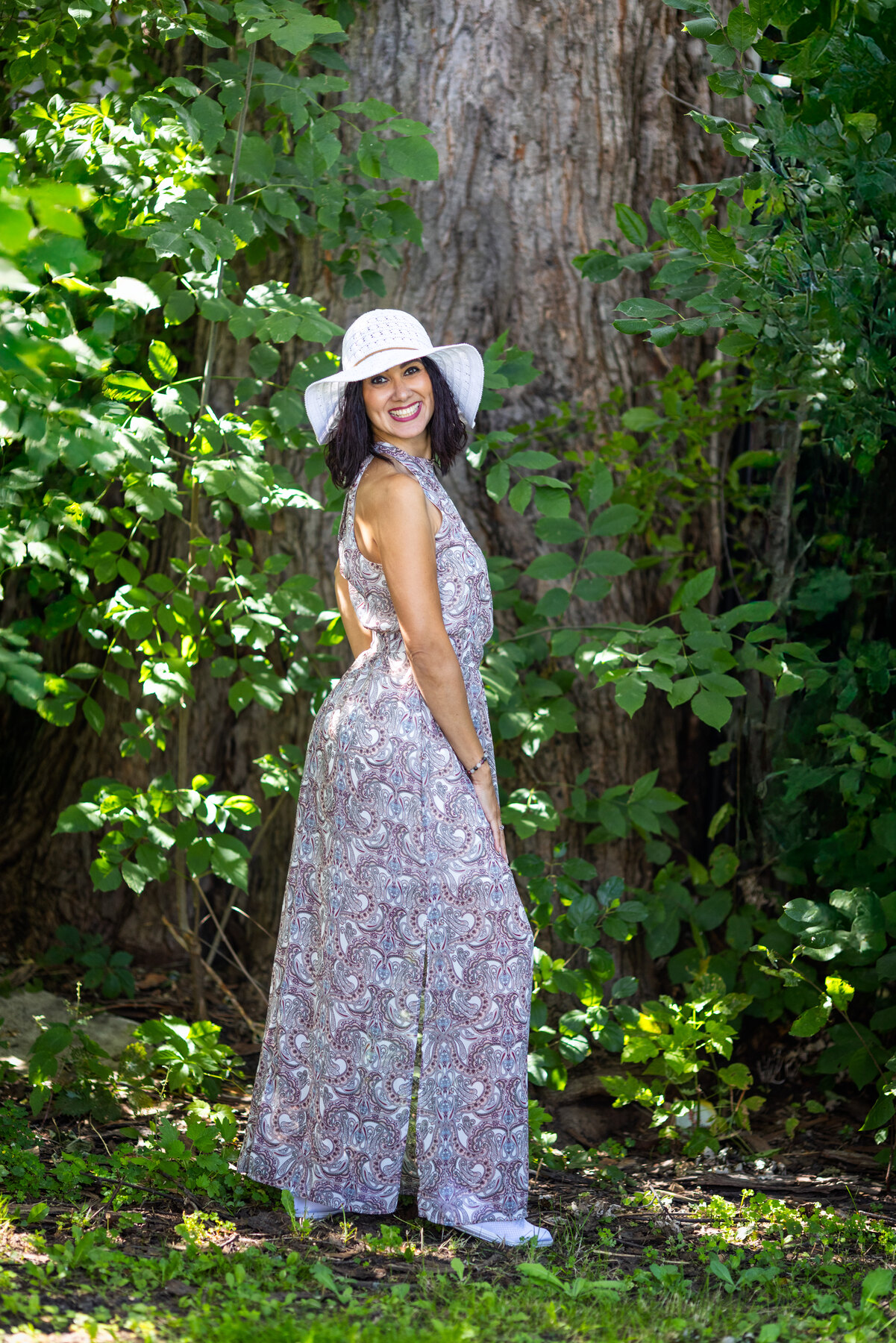 Rania in a patterned dress and sun hat under trees